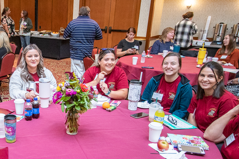 Four early educators smile around a table with flowers at the Inn at Virginia Tech.