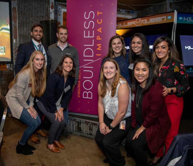 Several young alumni are posing in front of a banner during a networking event.